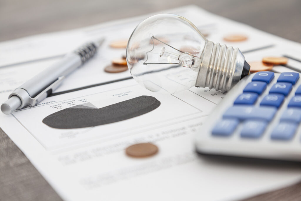 Closeup of bill and lightbulb with pennies showing higher electricity bill caused by inefficient air conditioning.
