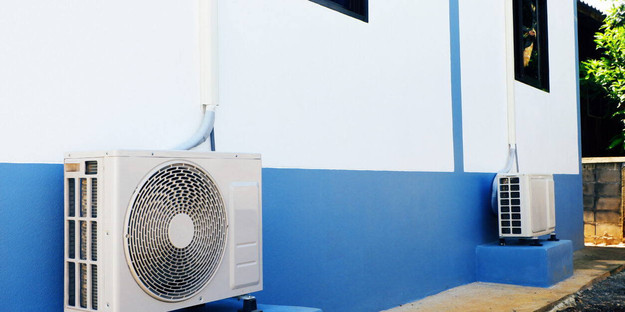 technology and motor pump A pair of mini-split AC outdoor units or heat pump condensers sitting on blue platforms against a white and blue exterior wall of a building, illustrating the equipment that JC Melton can service.