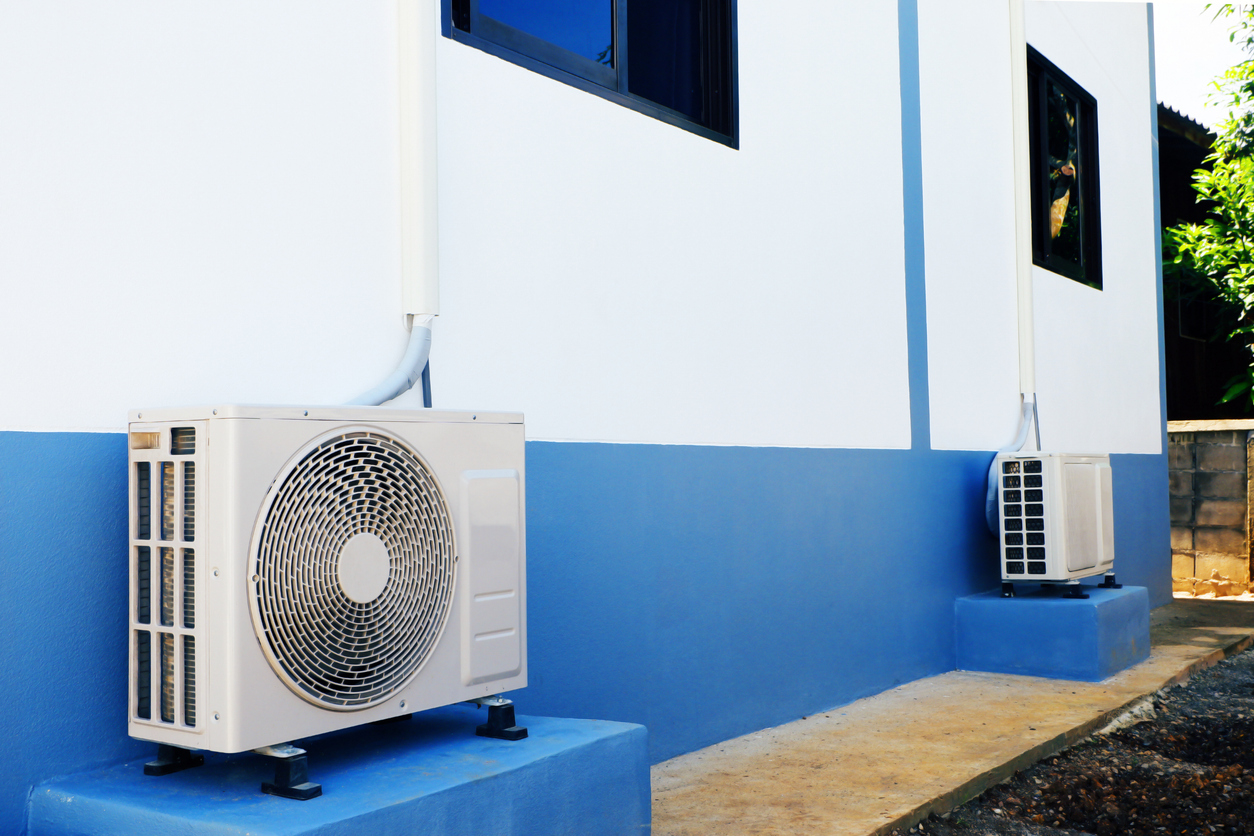 technology and motor pump A pair of mini-split AC outdoor units or heat pump condensers sitting on blue platforms against a white and blue exterior wall of a building, illustrating the equipment that JC Melton can service.